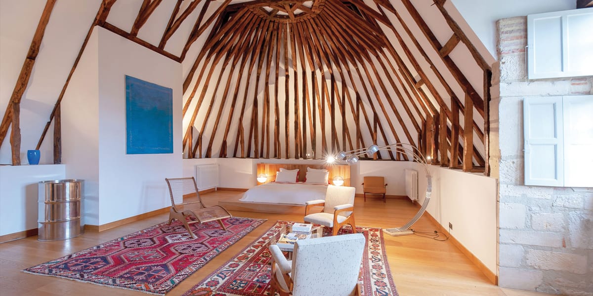 Guest suite with vaulted white timber ceiling, mid-century furniture, blue artwork, and stone walls
