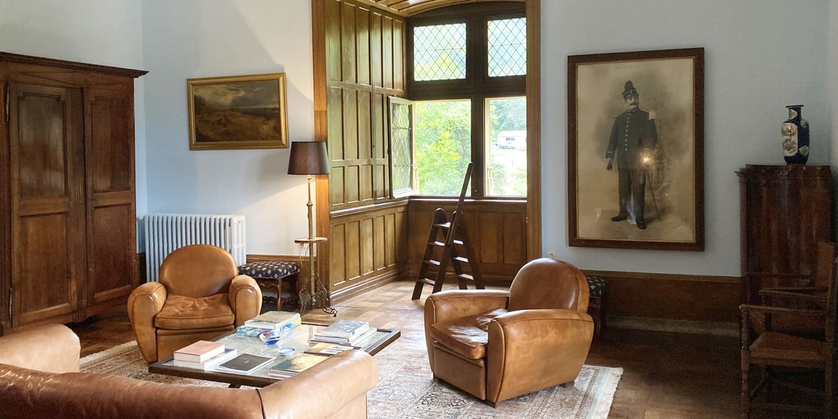 Chateau sitting room with dark oak paneling, leaded windows, tan leather chairs, and antique armoire