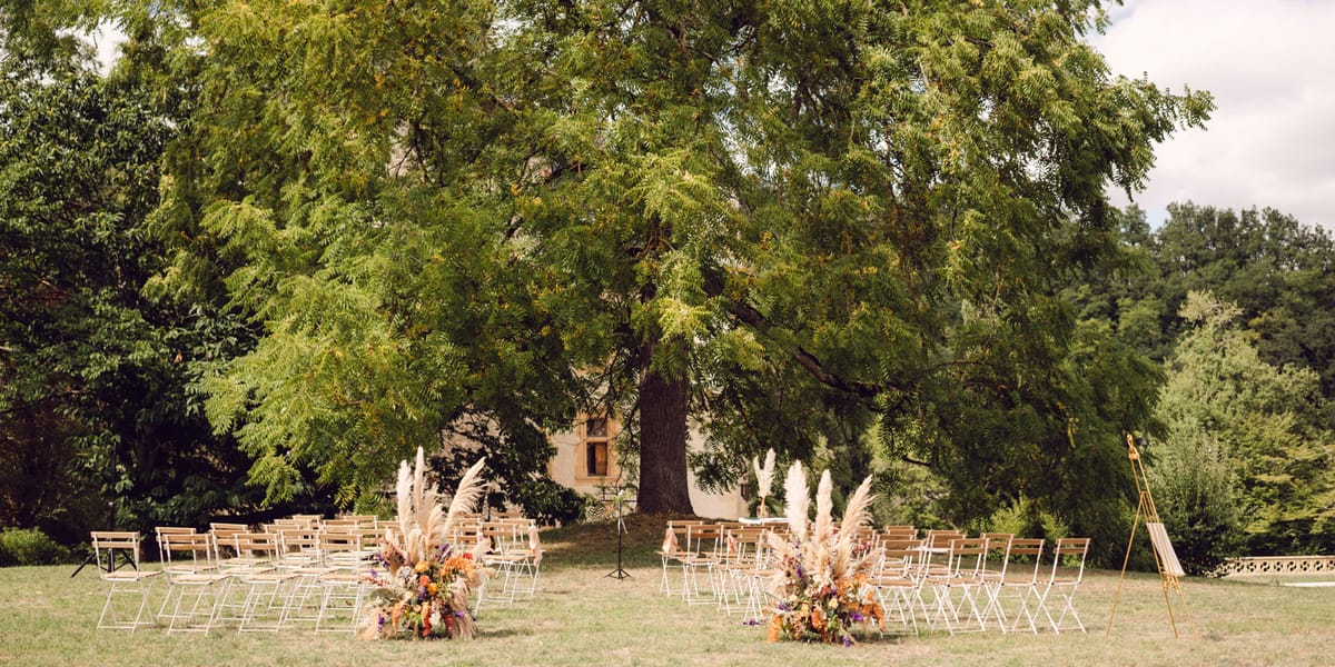 Outdoor ceremony setup with pampas grass and rust wildflower arrangements before stone manor on lawn