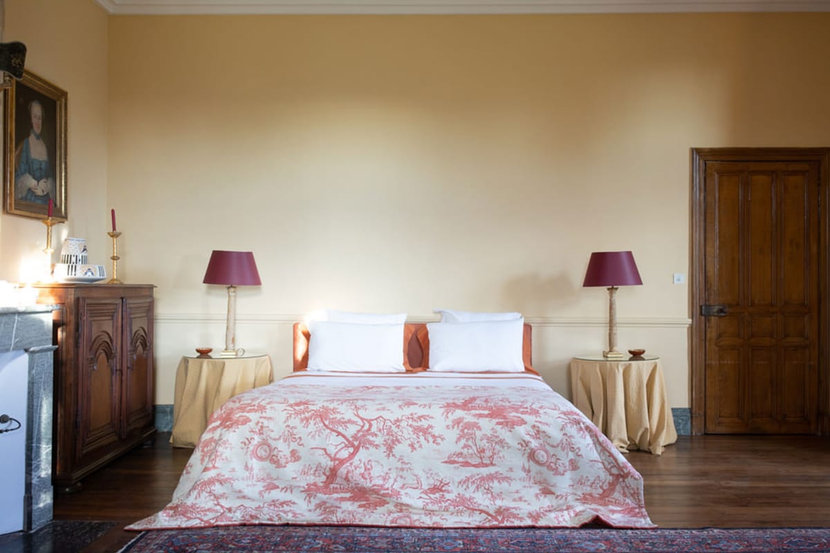 Chateau bedroom with toile de Jouy bedspread, ochre walls, marble fireplace, and walnut armoire