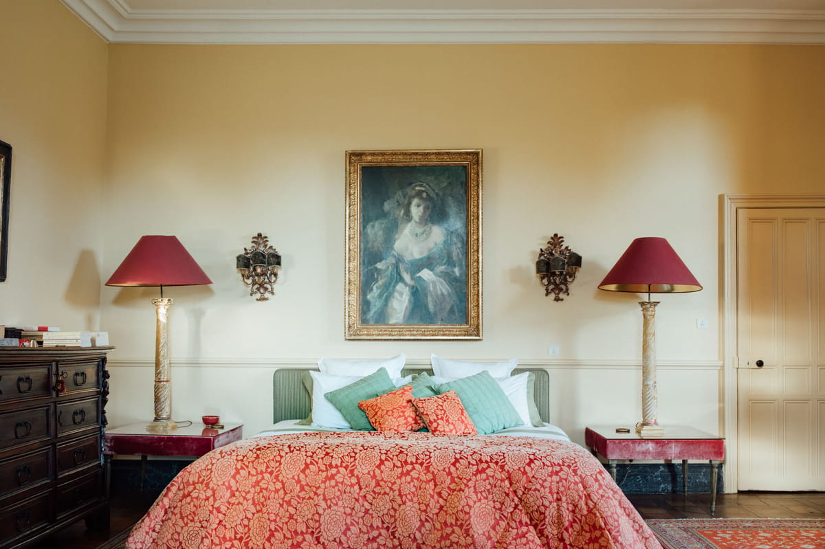 Chateau bedroom with red damask bedspread green headboard gilt portrait Persian rug and wrought iron chandelier
