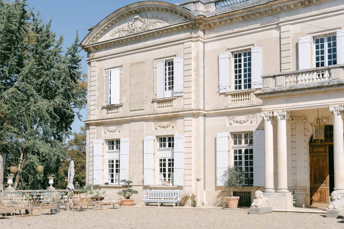 Limestone chateau with pediment coat of arms, sphinx sculptures, blue bench, and terracotta planters