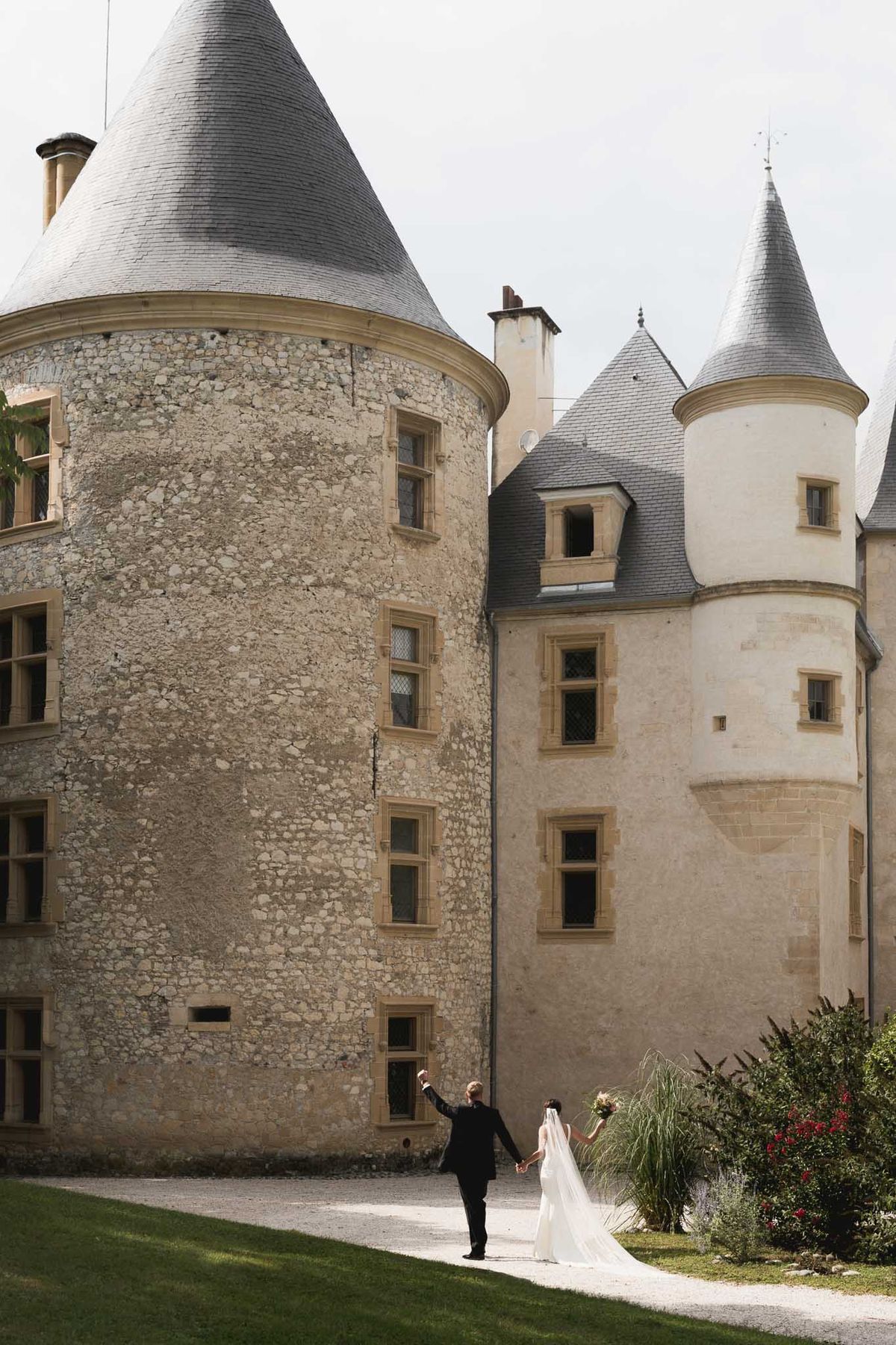 Bride and groom walking hand-in-hand across courtyard at historic French château with conical turrets