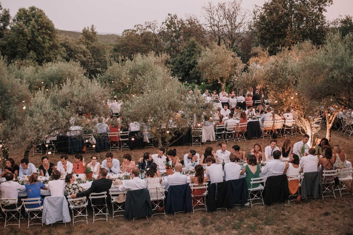 Elevated dusk view of reception dinner among olive trees with globe string lights and fairy-lit trunks