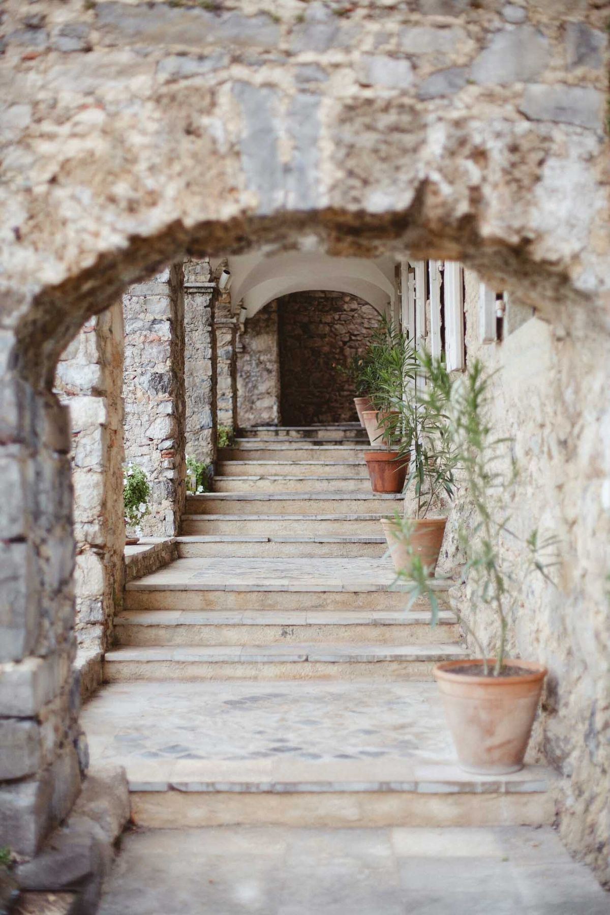 Stone staircases through successive arched passageways with terracotta pots and mosaic-tiled landings