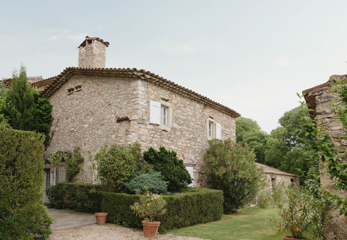 Traditional French stone mas with terracotta roof tiles, white shutters, box hedging, and pink oleander shrubs