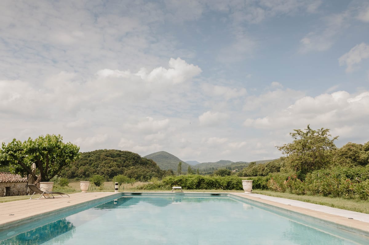 Rectangular pool with pale blue water stone paving Anduze urns and panoramic view of forested hills and valleys