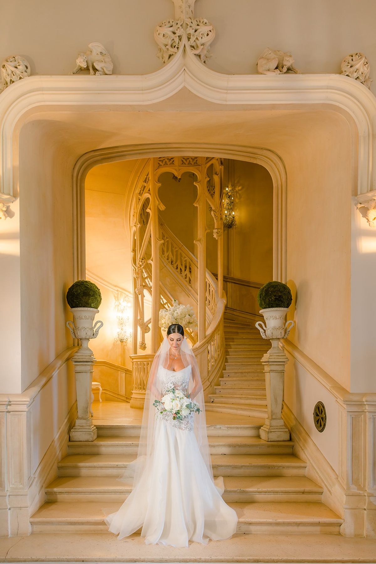 Bride on grand staircase with veil and bouquet at Chateau Challain, Loire Valley