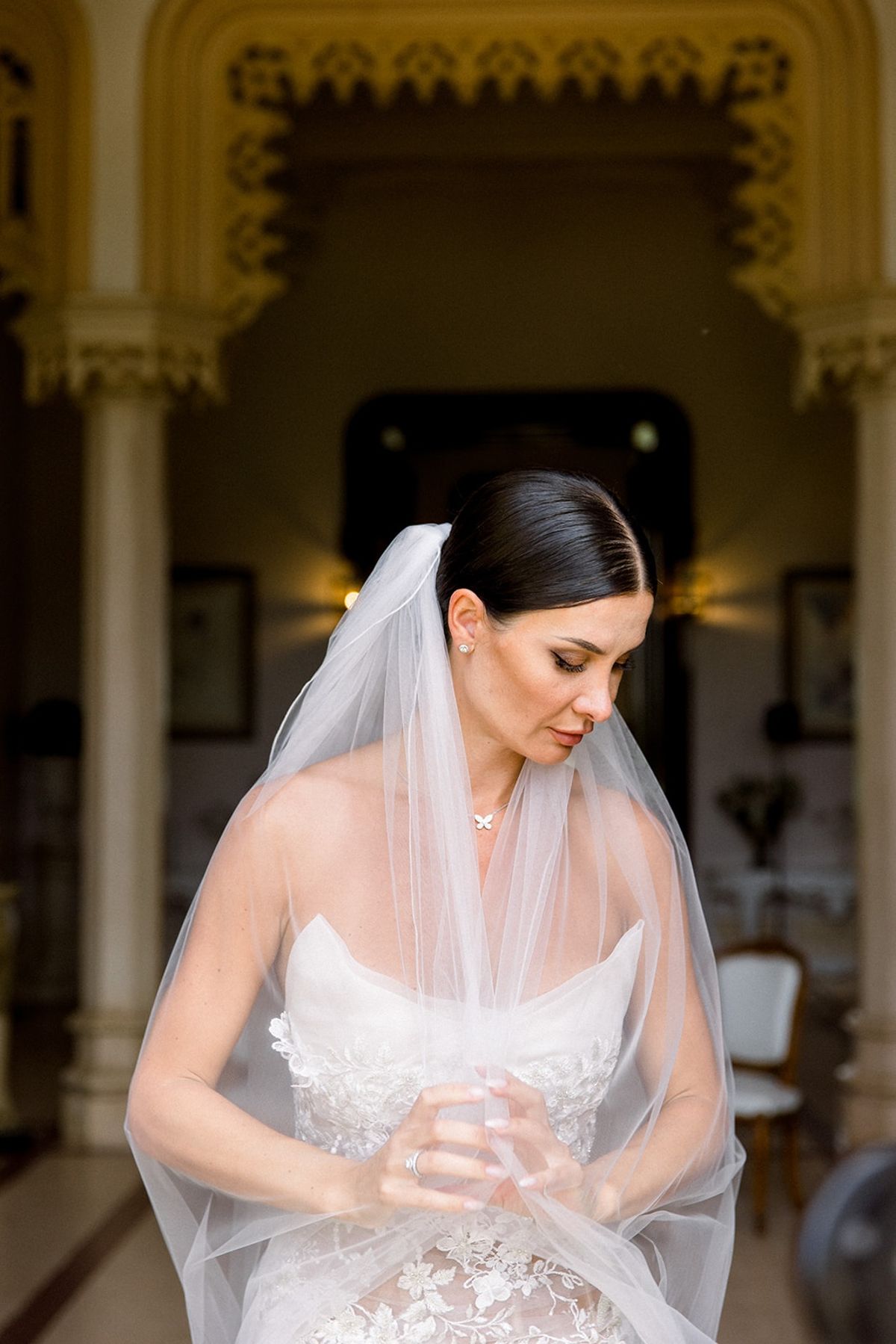 Bride in slick low bun and veil under Gothic columns at Chateau Challain, Loire Valley