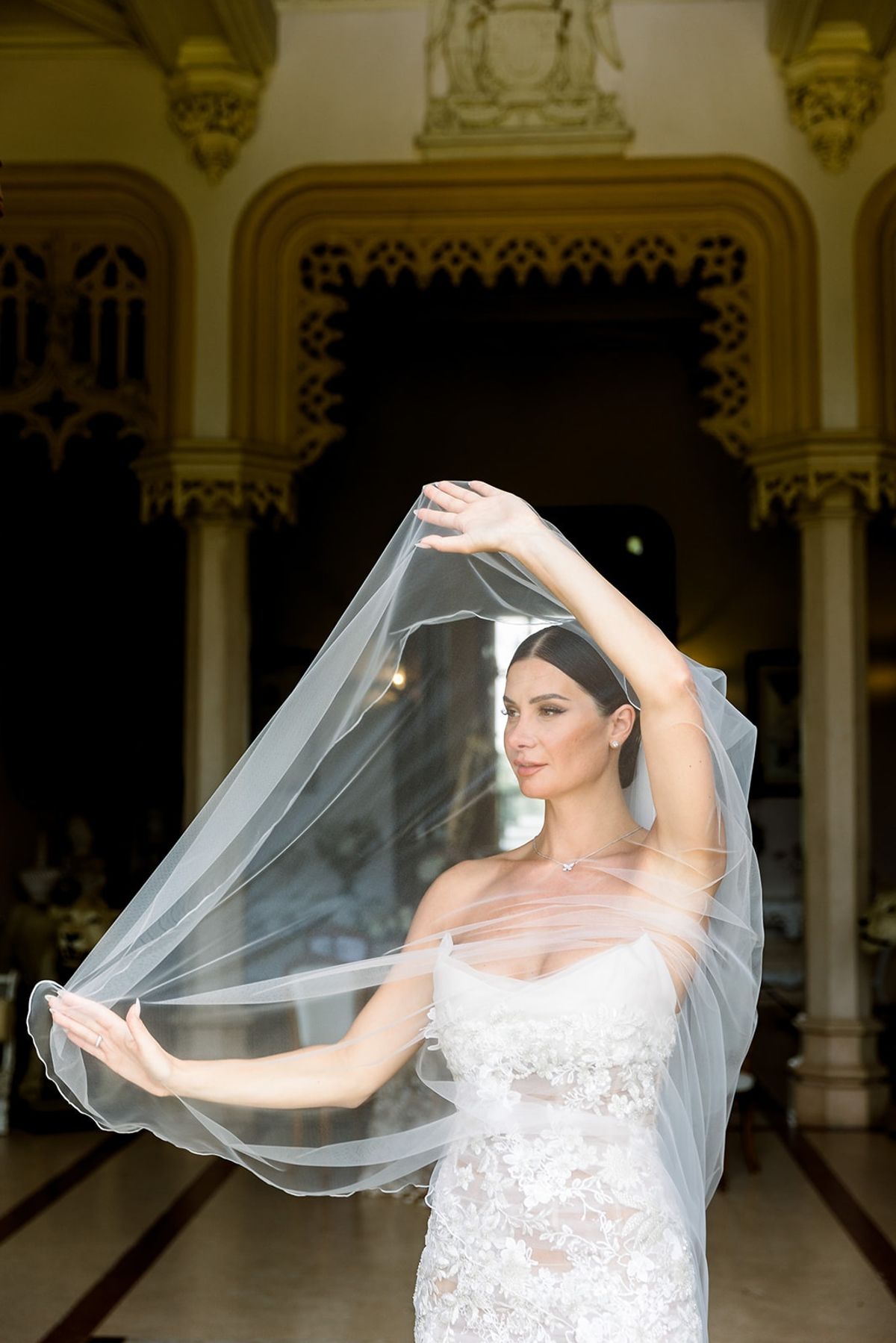Bride lifting tulle veil under gilded arch at Chateau Challain, Loire Valley