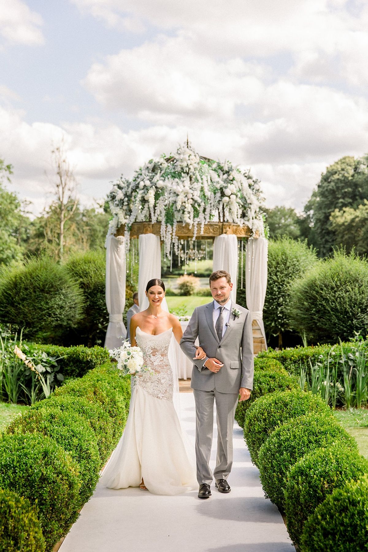 Couple walking down ceremony aisle from floral arch at Chateau Challain, Loire Valley