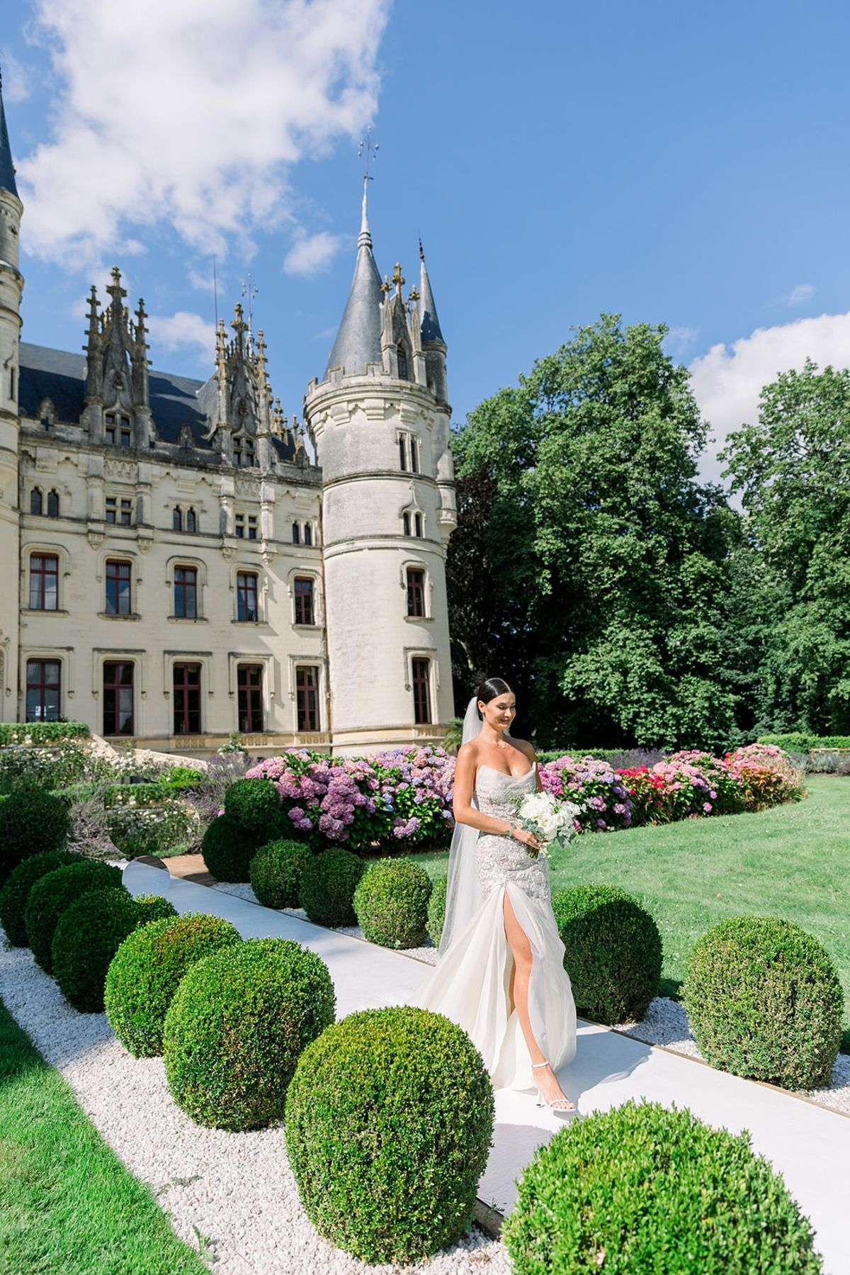 Bride walking beside chateau turret with bouquet at Chateau Challain, Loire Valley