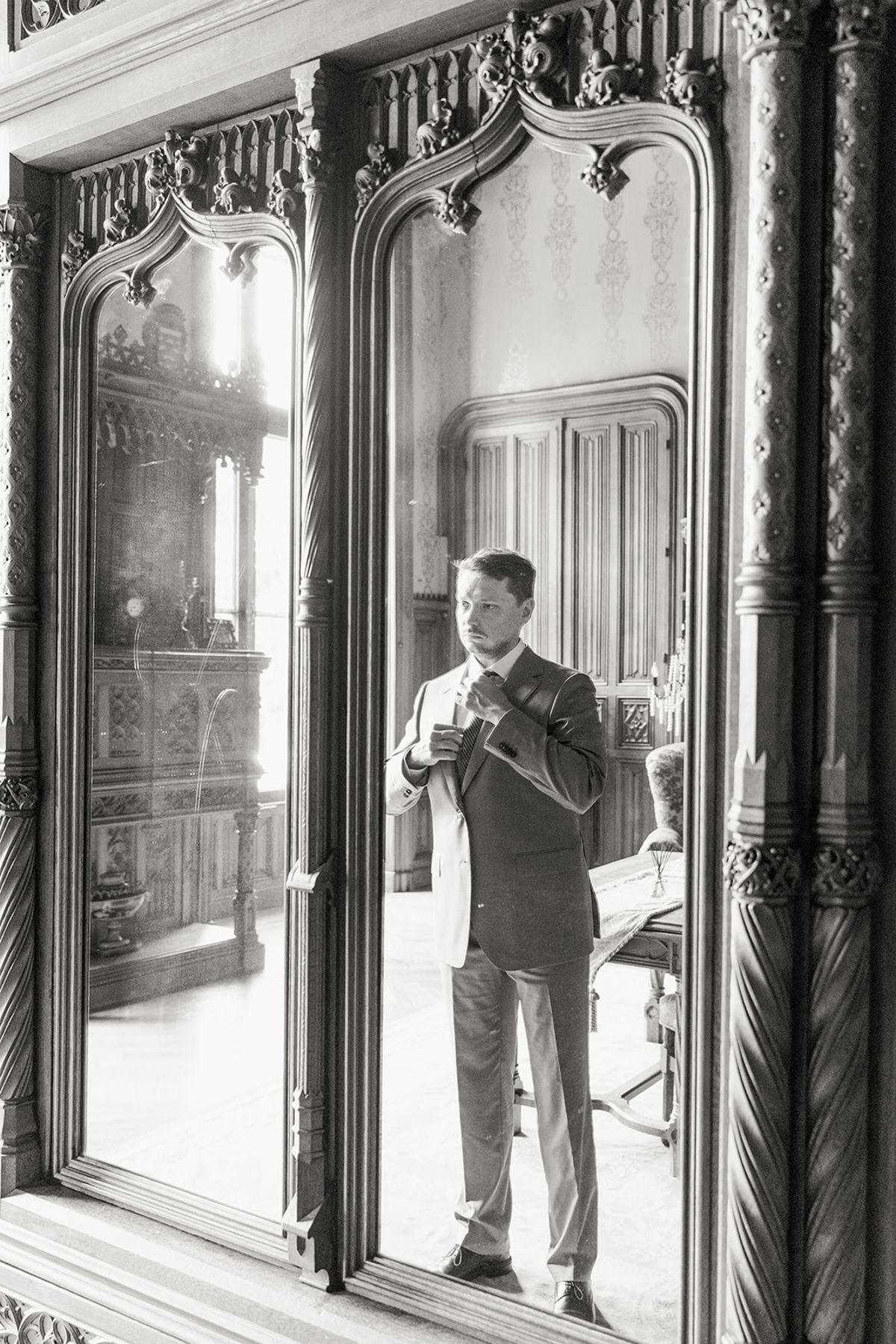 Groom adjusting tie before mirrored armoire at Chateau Challain, Loire Valley