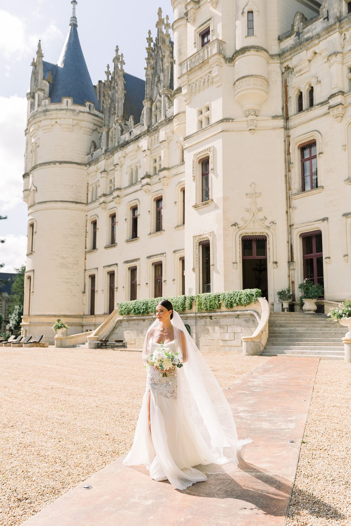 Bride with bouquet on chateau forecourt at Chateau Challain, Loire Valley