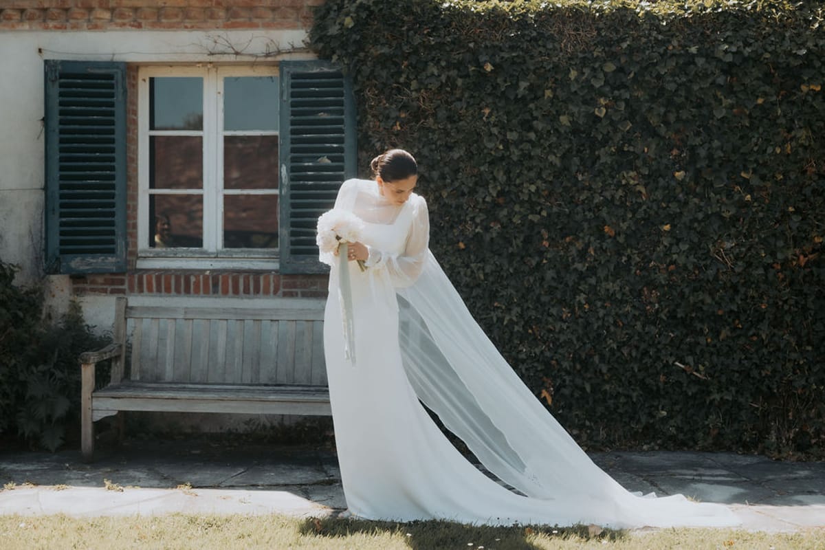 The bride in her veil in front of a shuttered window and an ivy-covered wall
