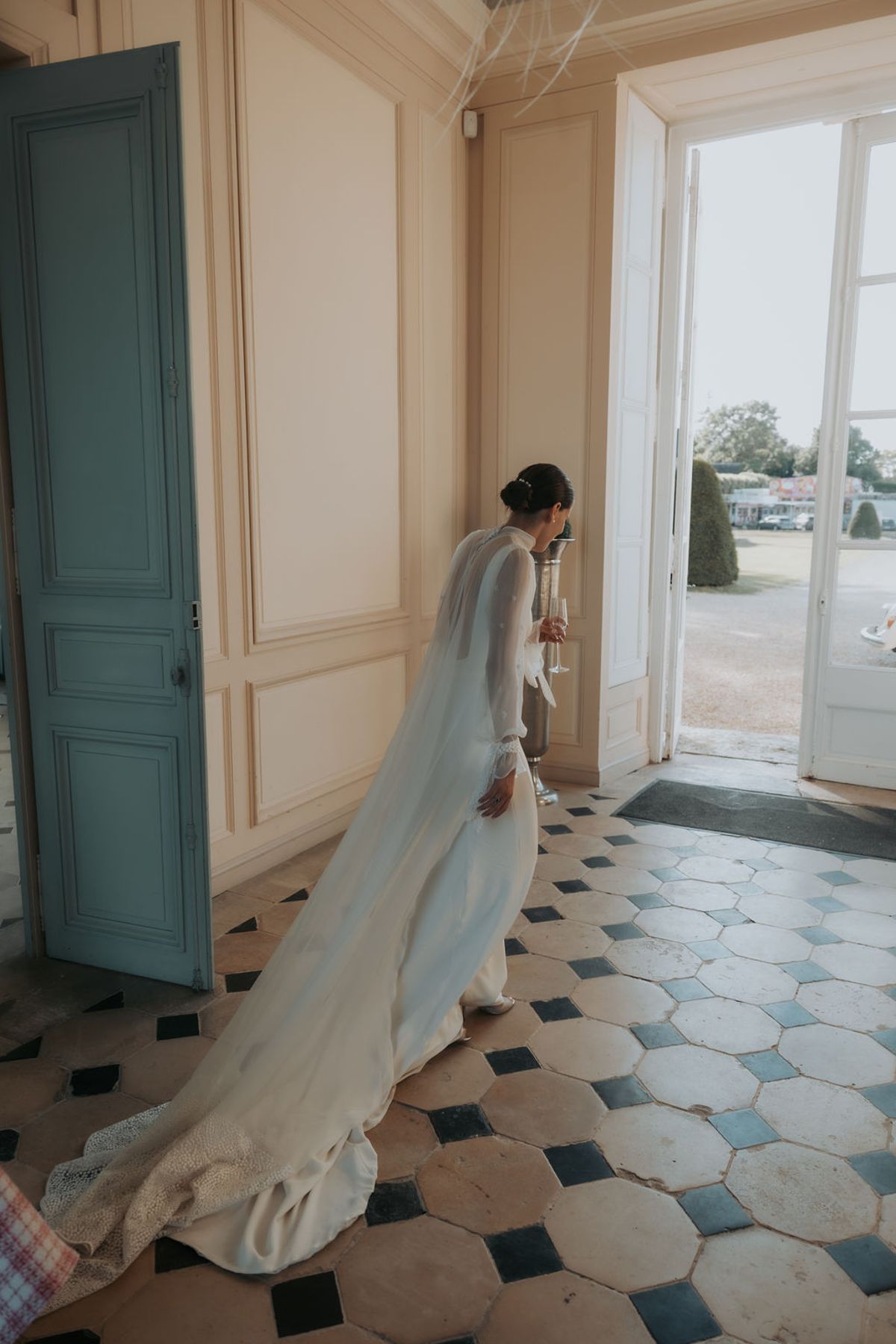 The bride steps through a tall open door onto a black and white tiled floor