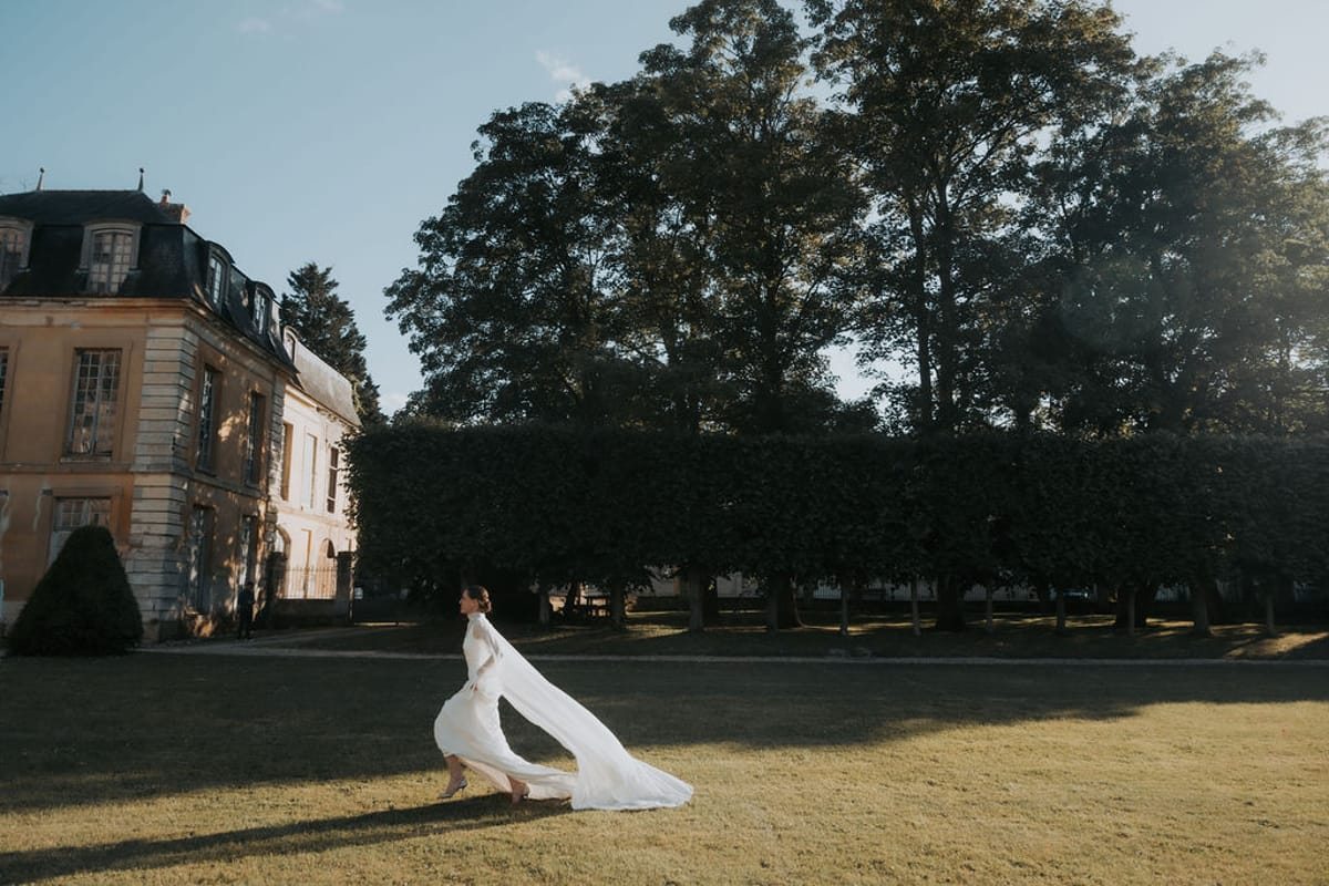 The bride on the lawn in front of the château, her veil spread behind her