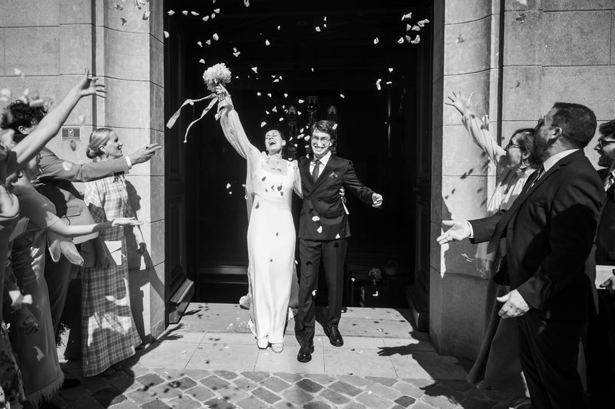 Guests throw petals as the bride and groom leave the church, in black and white