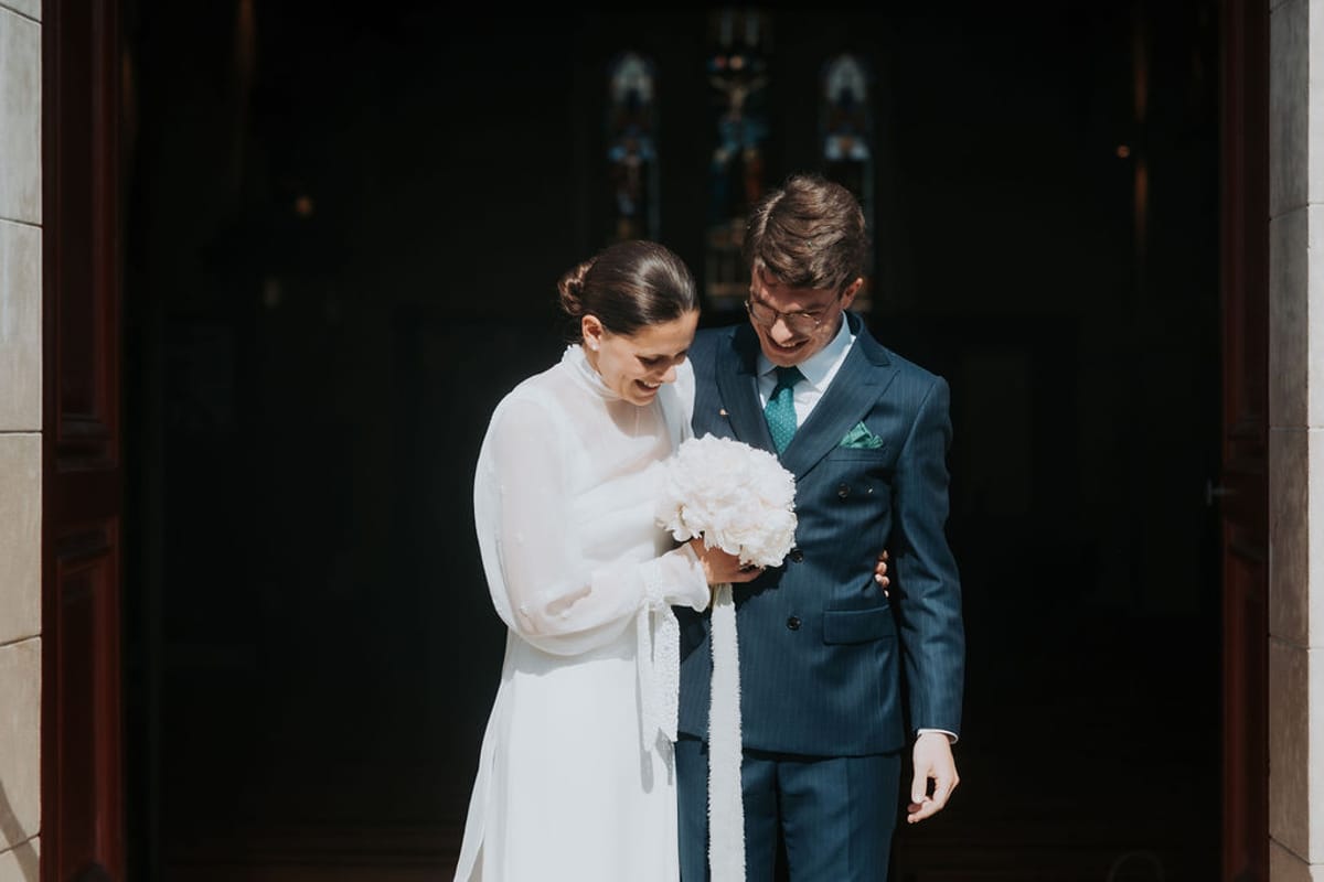 The bride and groom at the church door, the groom in a blue suit