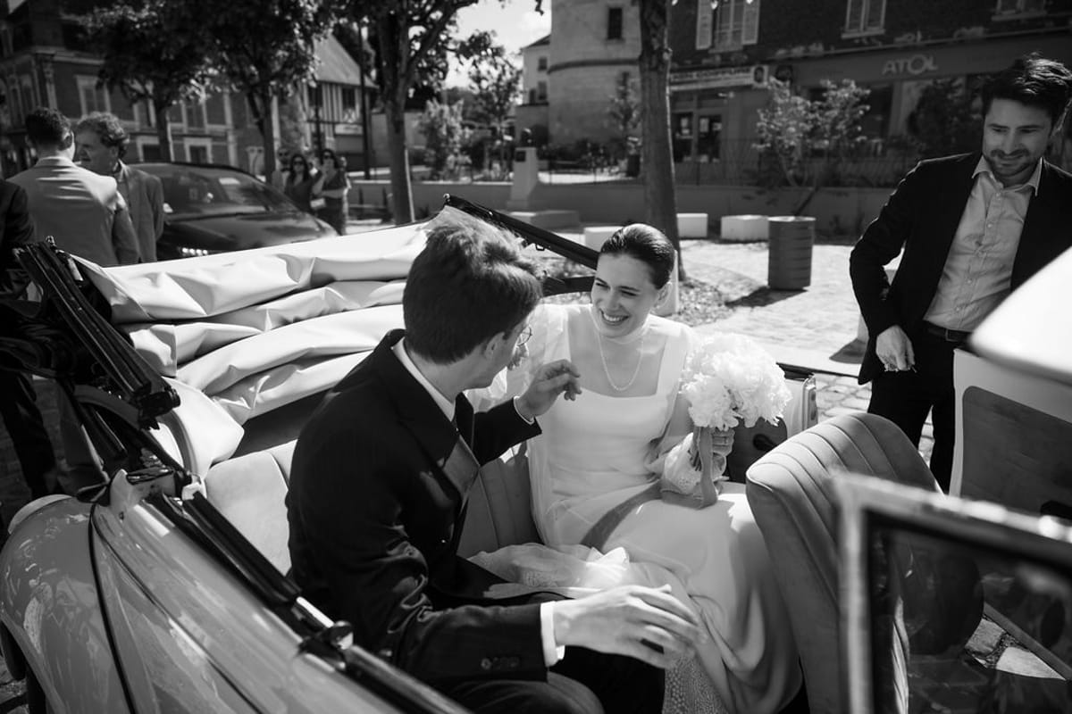 The bride and groom in the back of a vintage open-top car with guests around them