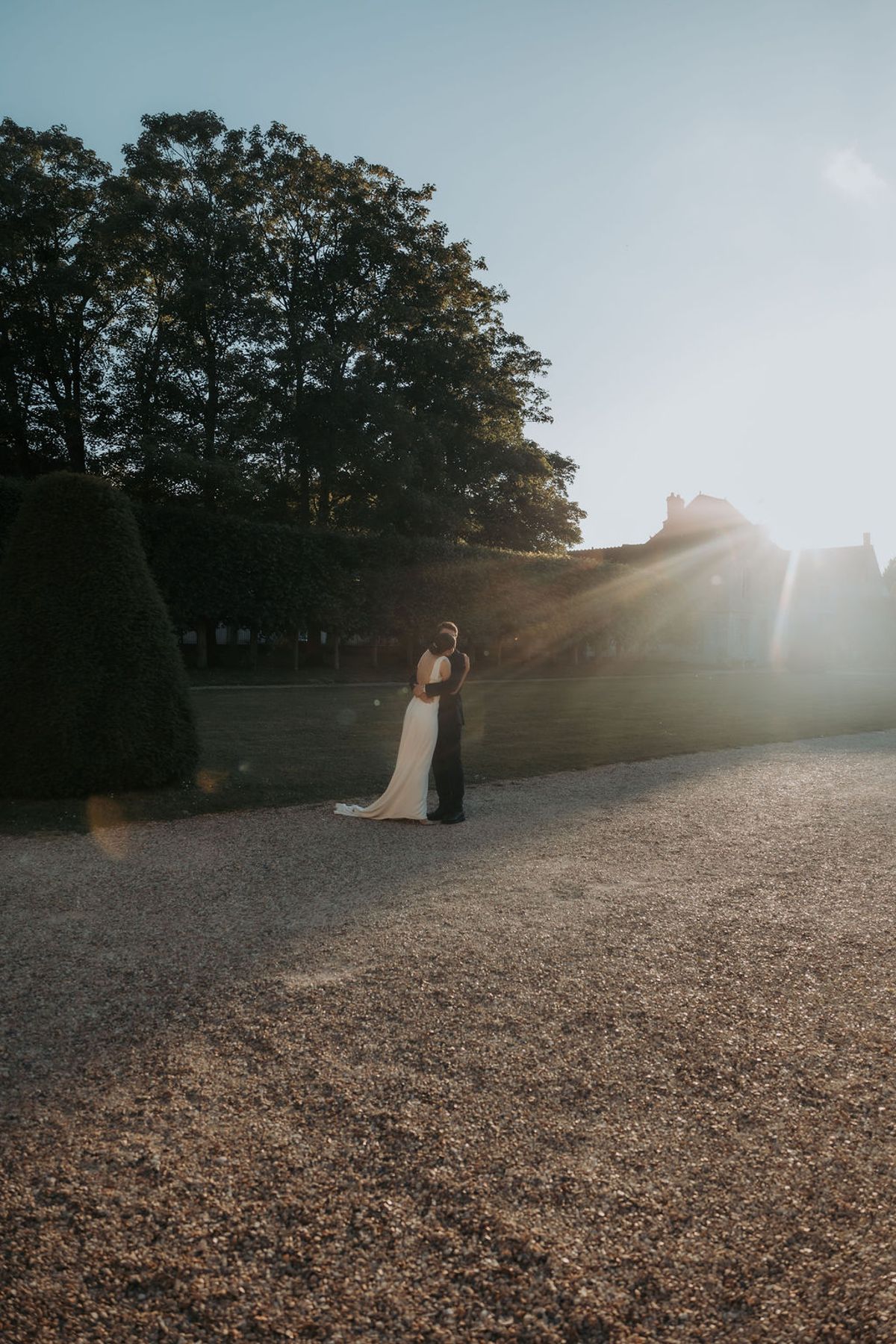 The bride and groom in the distance on the drive, framed by trees in the evening light