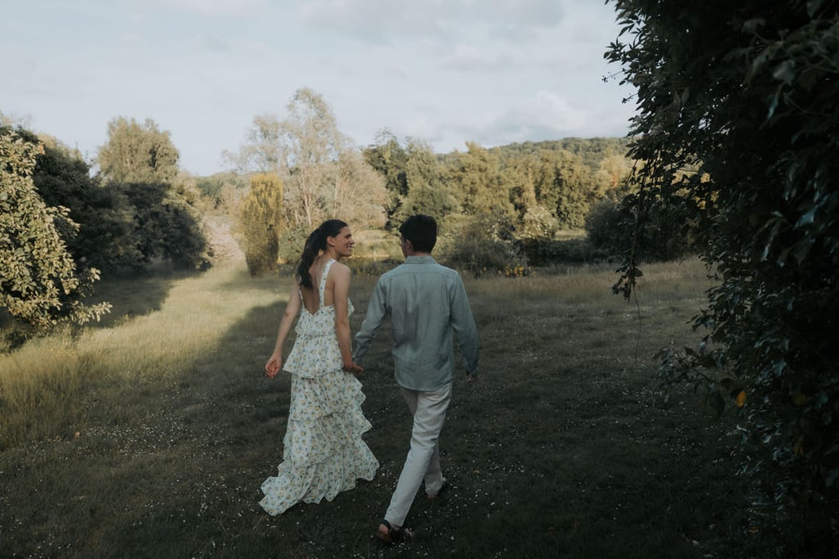 The bride and groom walk hand in hand through long grass