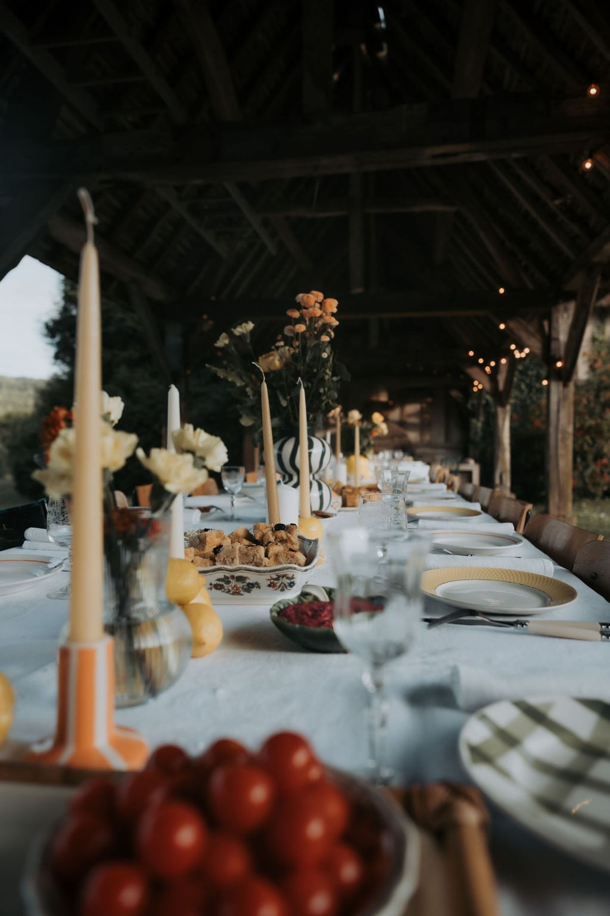 Candles, cherry tomatoes and flowers on a white tablecloth beneath the barn beams