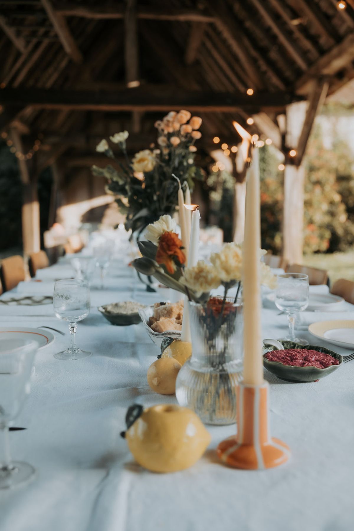 Orange and yellow flowers, tall candles and striped plates on the long table
