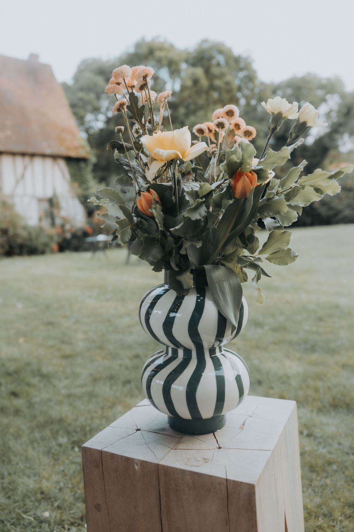 A bunch of garden flowers in a green and white striped vase on a wooden plinth