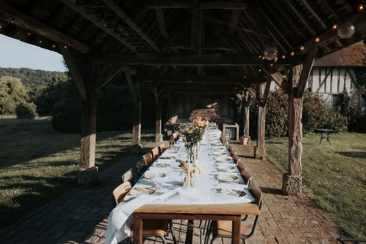 A long table laid with white linen beneath a timber barn roof