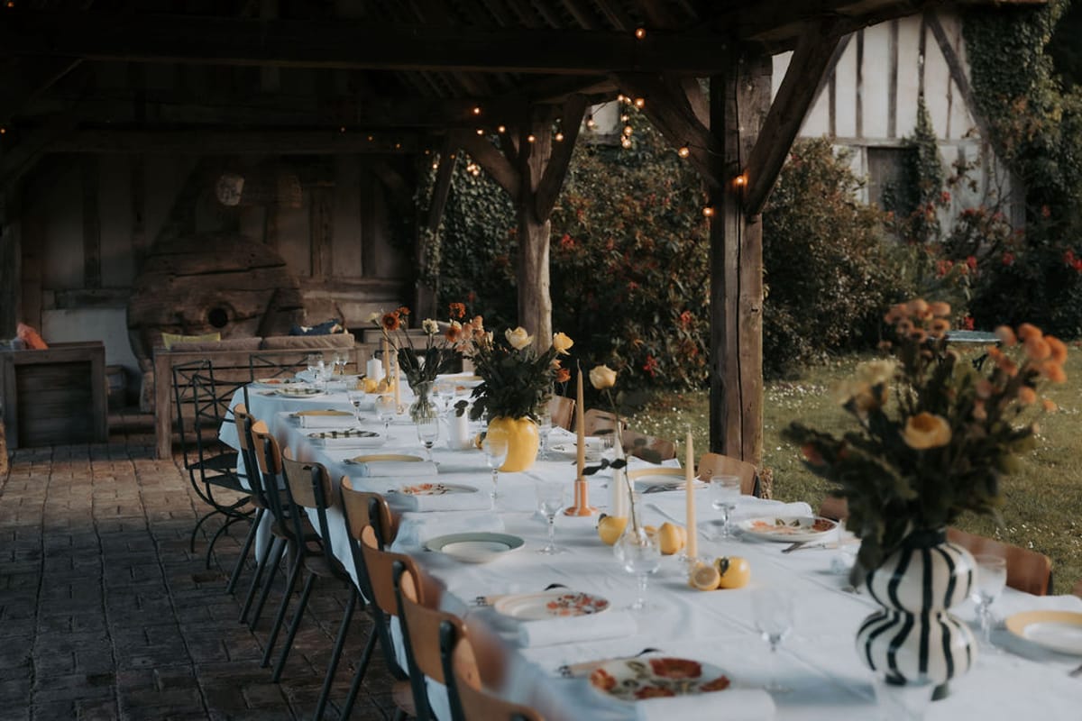 A long dinner table under an open timber barn, with flowers in striped vases
