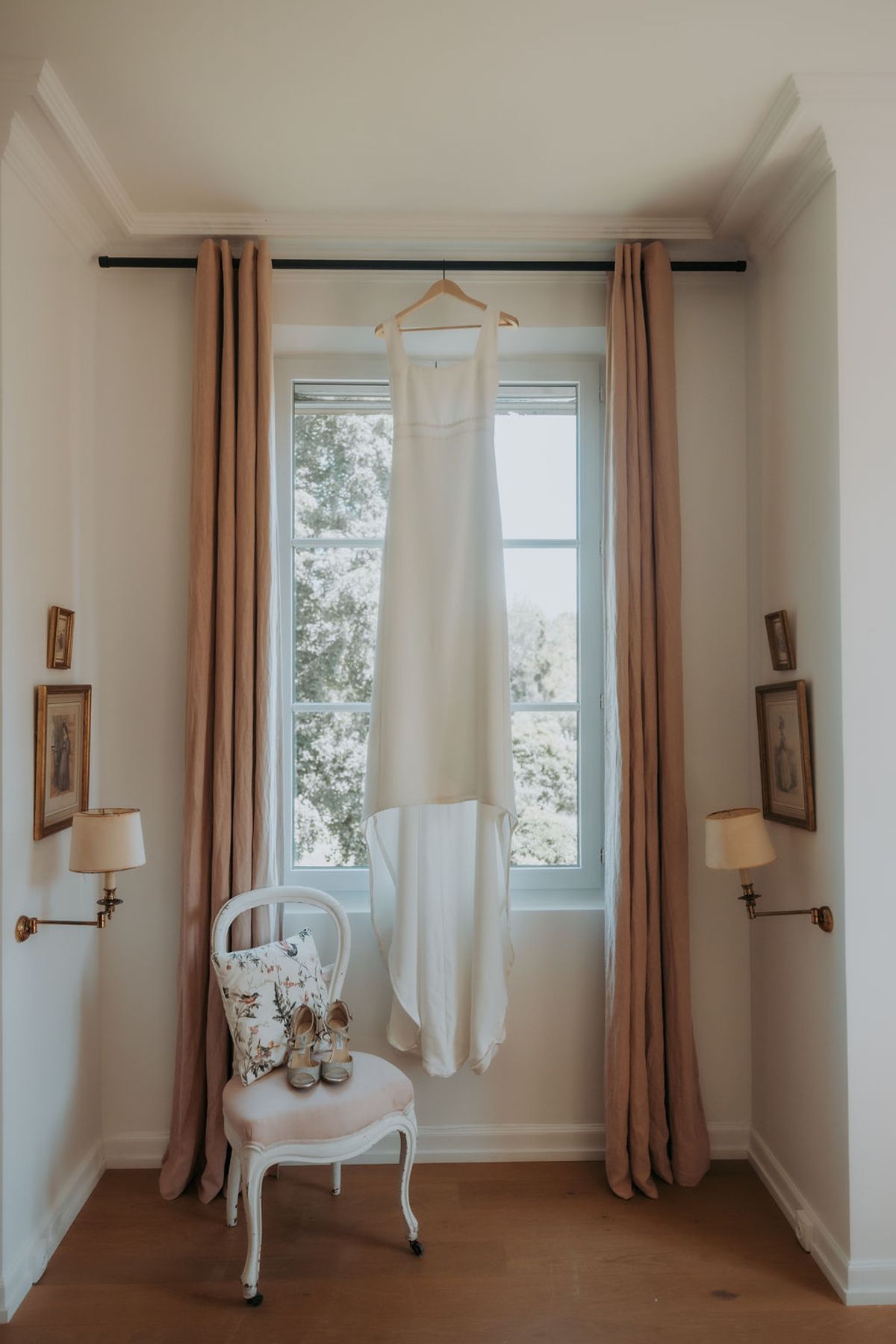 The wedding dress hanging in a window between long curtains