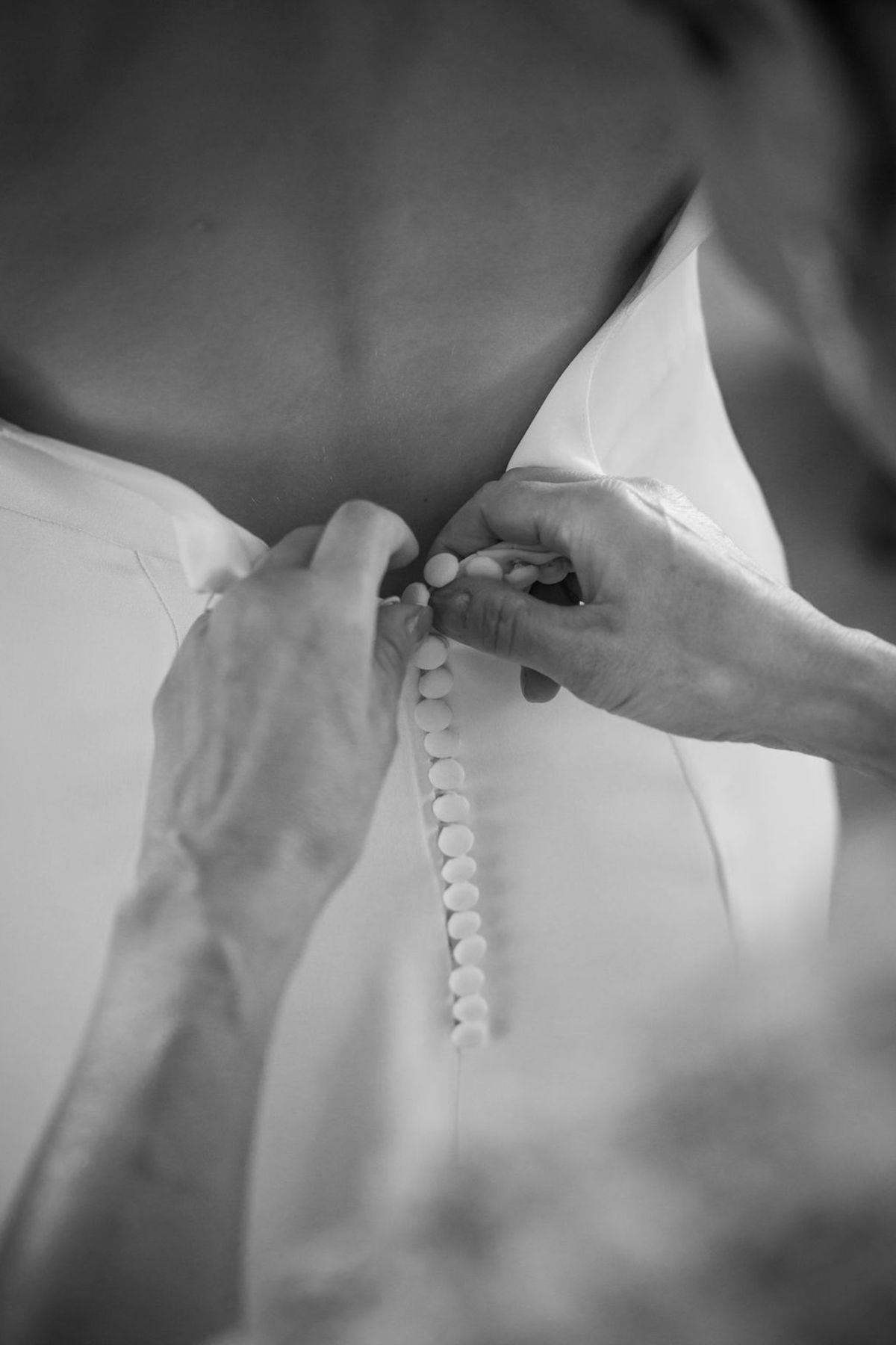 Hands fastening the row of buttons on the back of the dress, in black and white