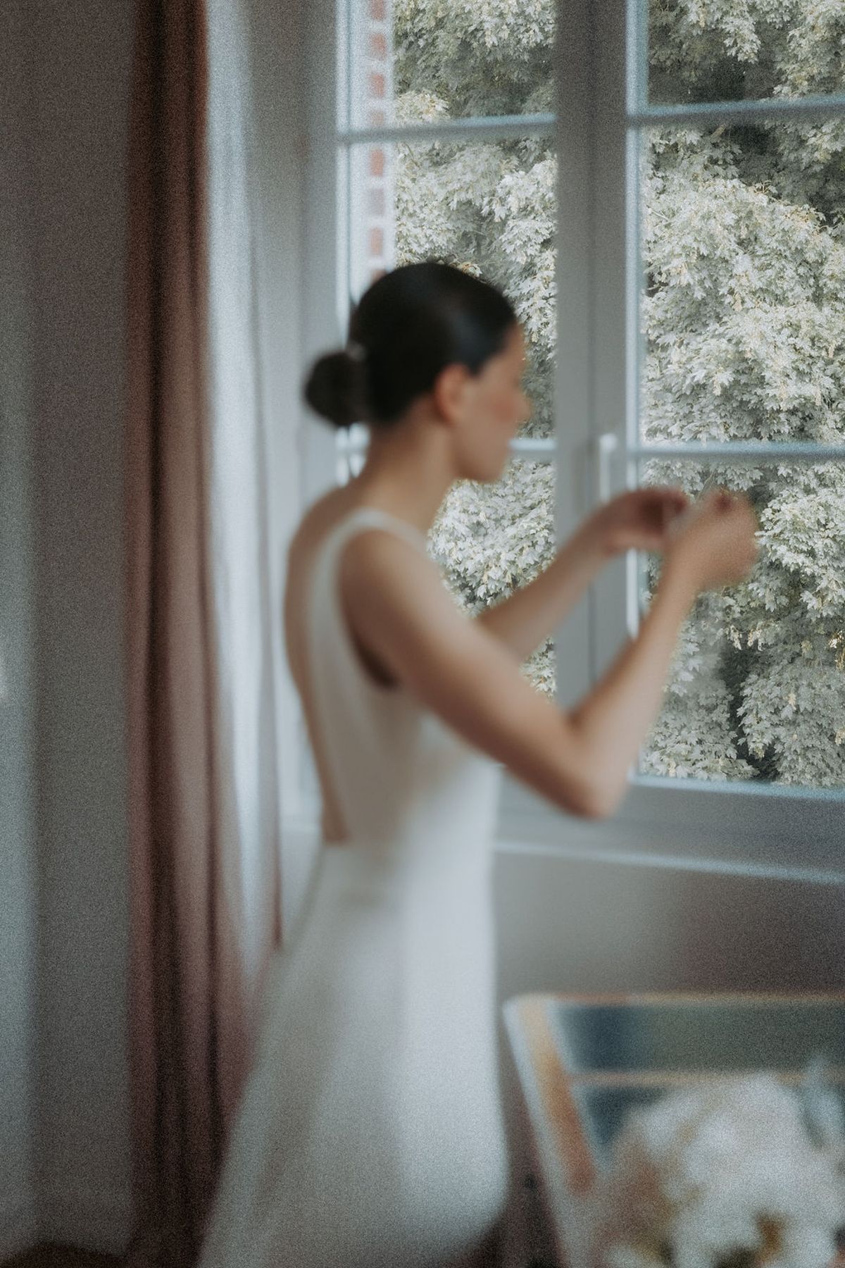 The bride adjusting her earring by a tall window
