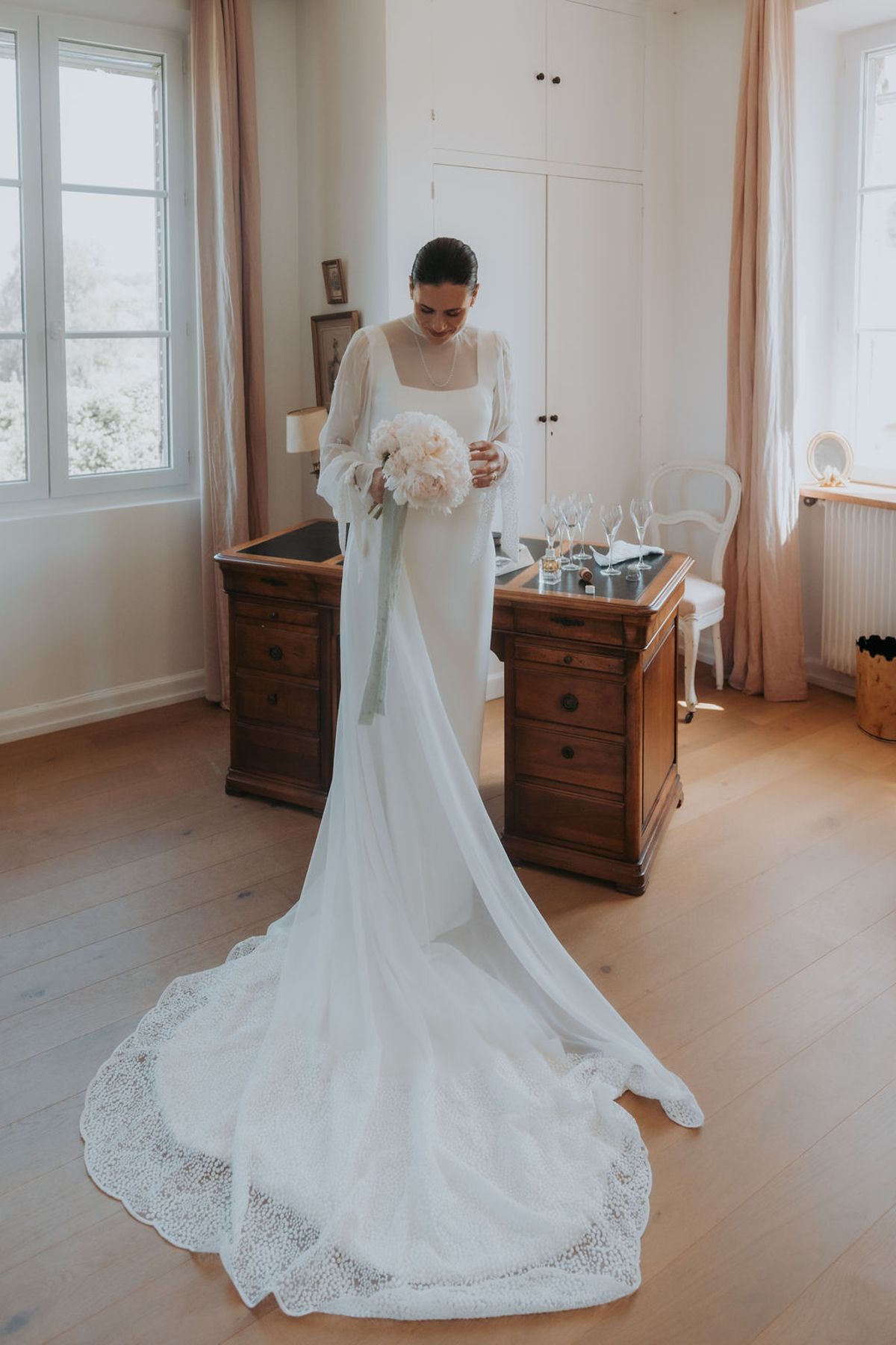 The bride in her long-sleeved dress and cathedral veil in a bedroom