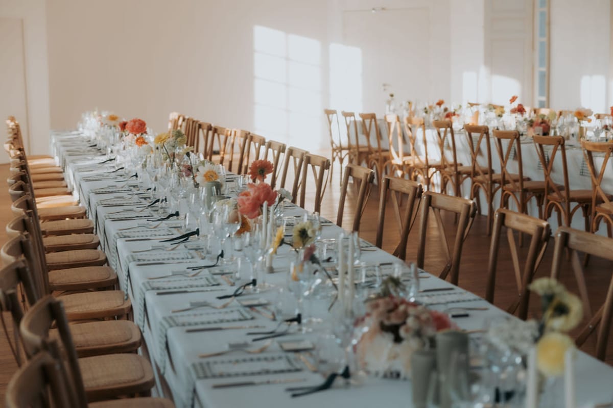 Long tables with wooden chairs, white linen and small bunches of flowers
