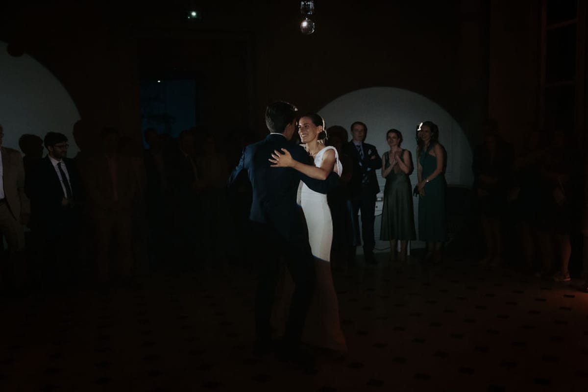 The bride and groom dance in a dark room surrounded by guests