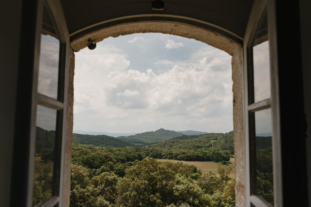 Panoramic valley view through open stone arch window in historic chateau with forested hills beyond