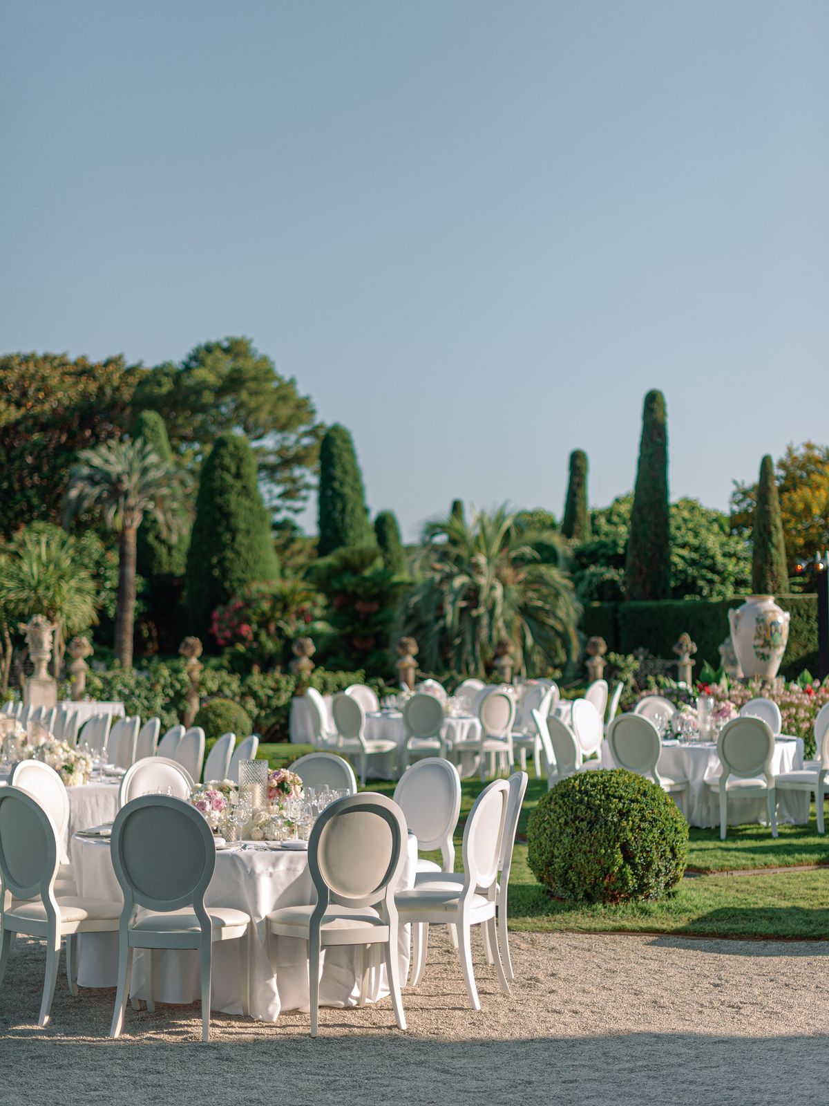 Outdoor wedding reception with round tables in white linen and blush floral centerpieces on a formal French garden terrace