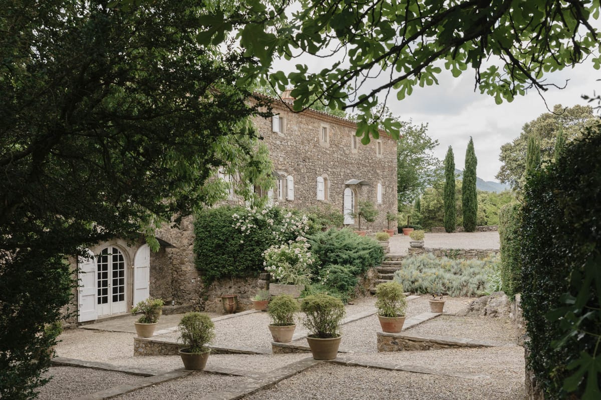 Provencal stone mas with white shutters, topiary in terracotta pots, and cypress trees on gravel forecourt