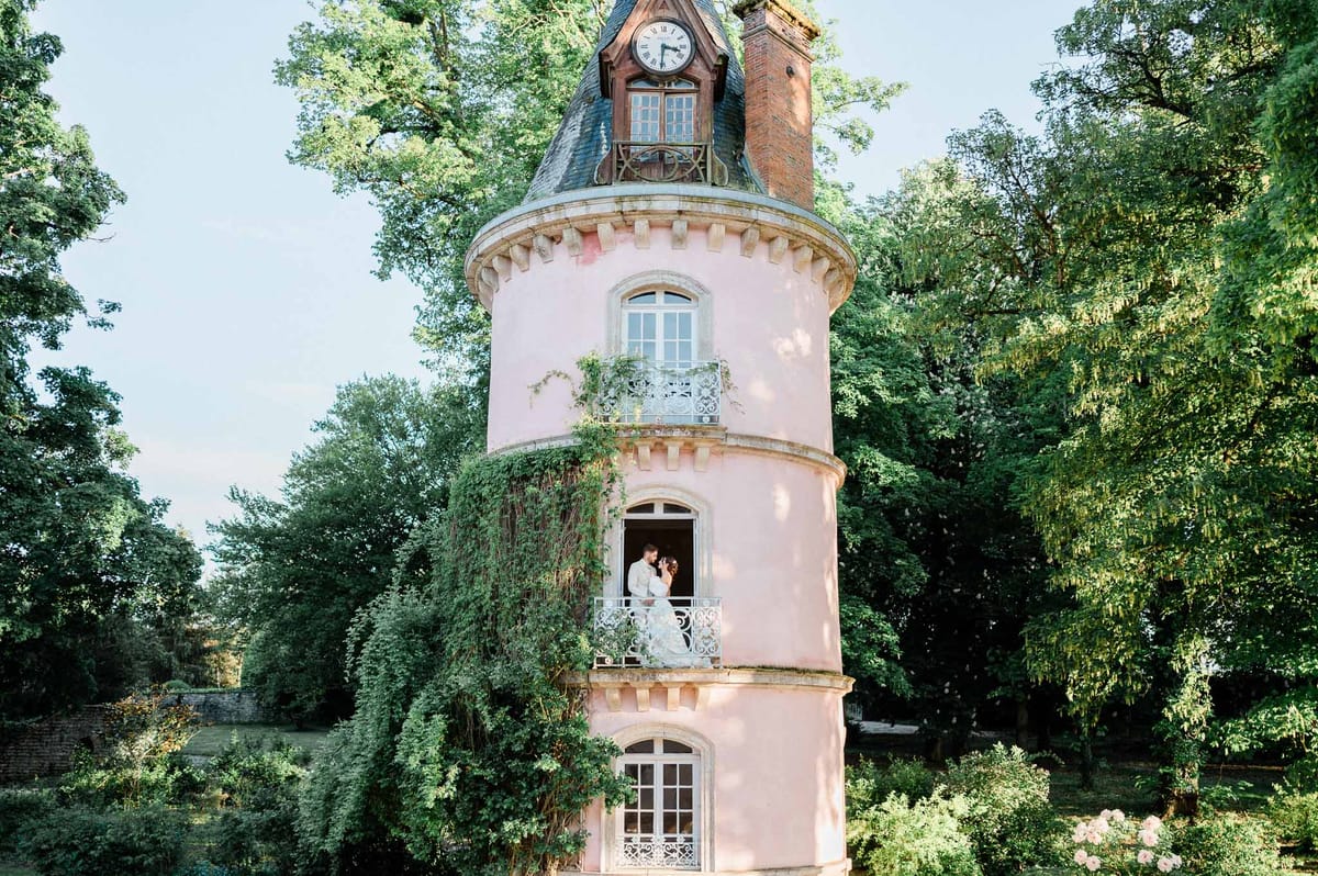Bride and groom on pink tower balcony surrounded by woodland at historic wedding venue