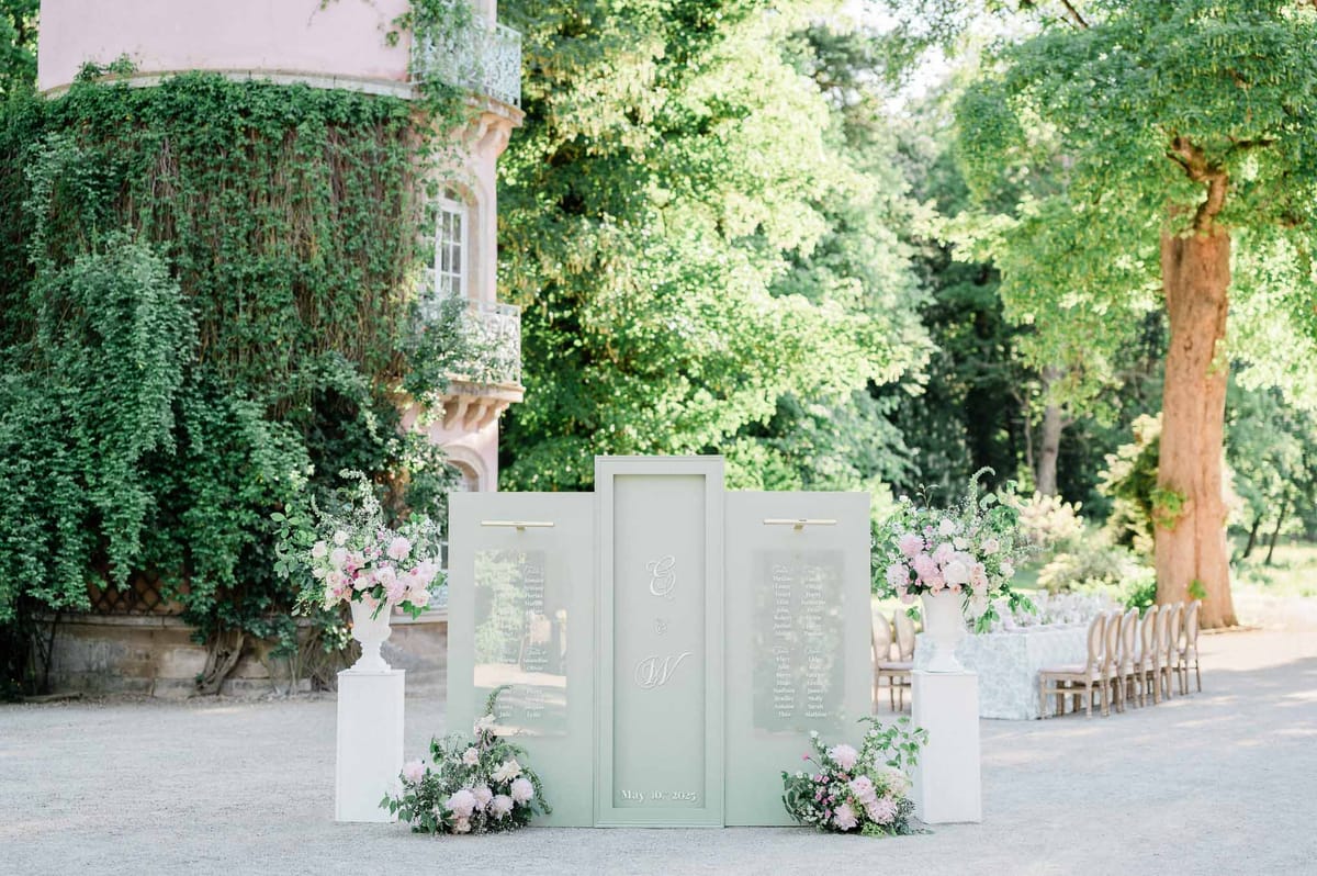 Outdoor ceremony seating chart with sage green panels and pink peonies in ivy-covered courtyard