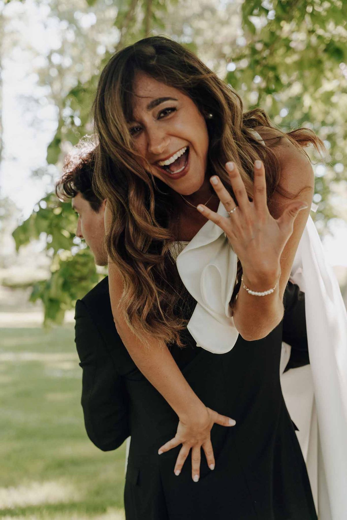 Candid portrait of bride on groom's back showing wedding rings and tennis bracelet in garden setting