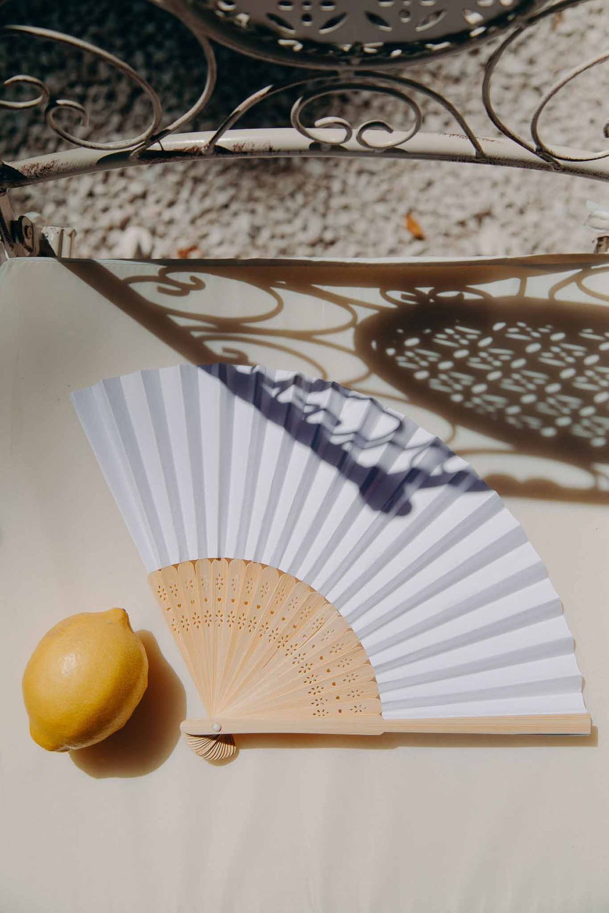 White striped paper hand fan with bamboo handle and lemon styled as wedding favour in natural sunlight