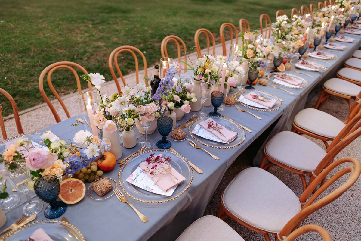Elevated view of a dusty blue reception tablescape with gold-rimmed chargers, cobalt goblets, and garden-style floral runner