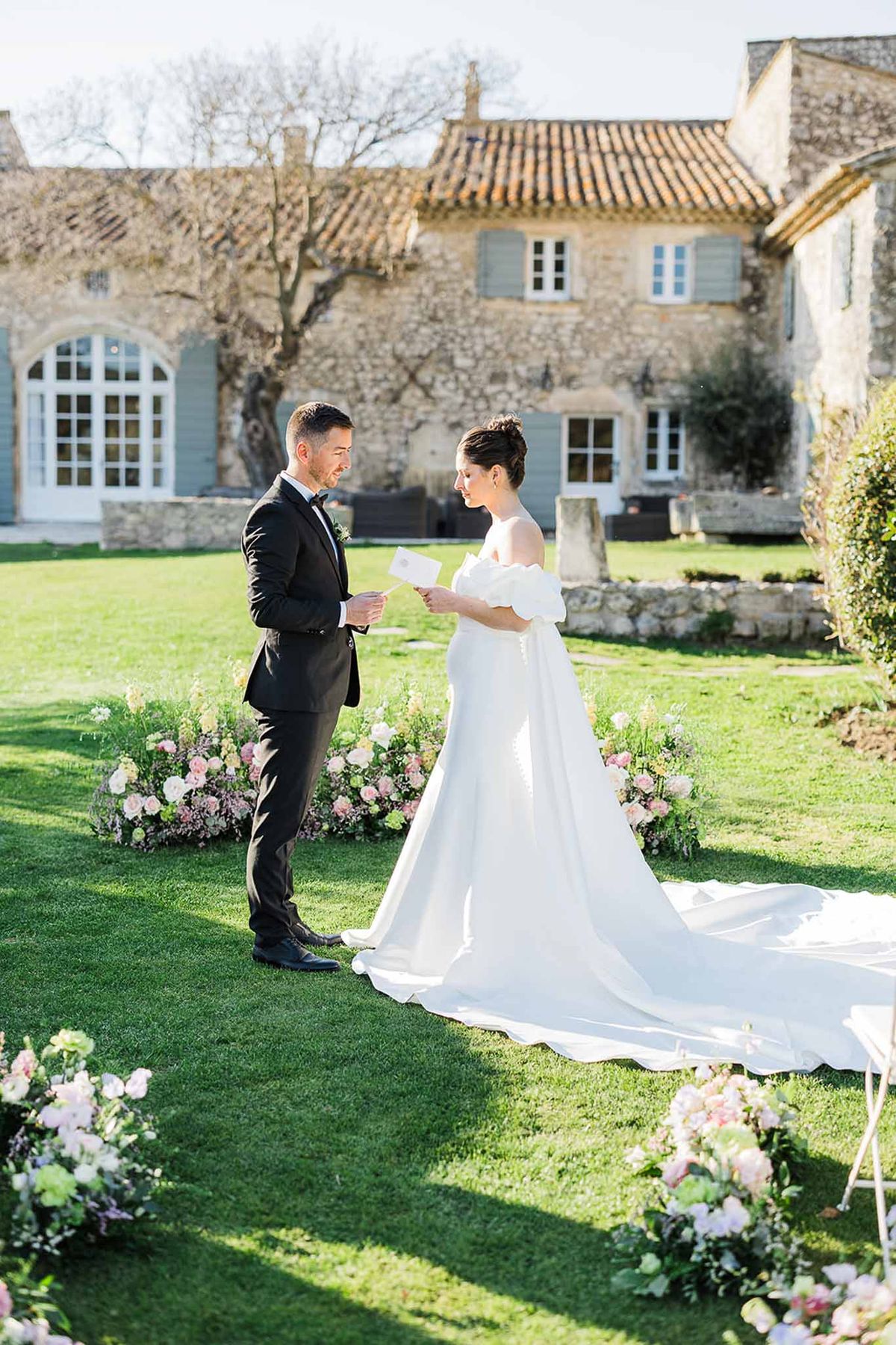 Bride and groom exchanging vows during outdoor ceremony at French stone manor house with floral arrangements