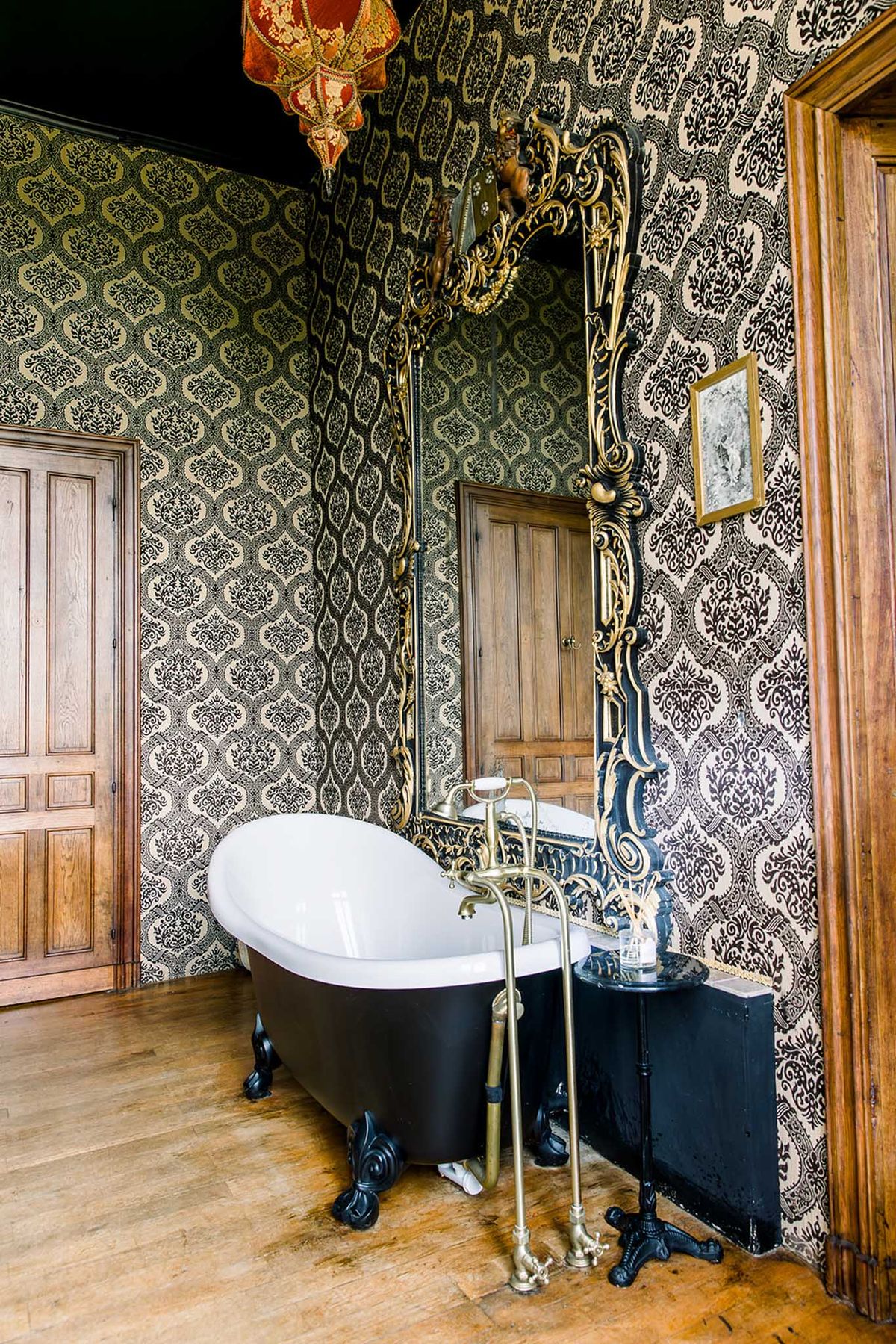 Theatrical bathroom with black clawfoot tub, baroque gold mirror, and damask wallpaper in two patterns