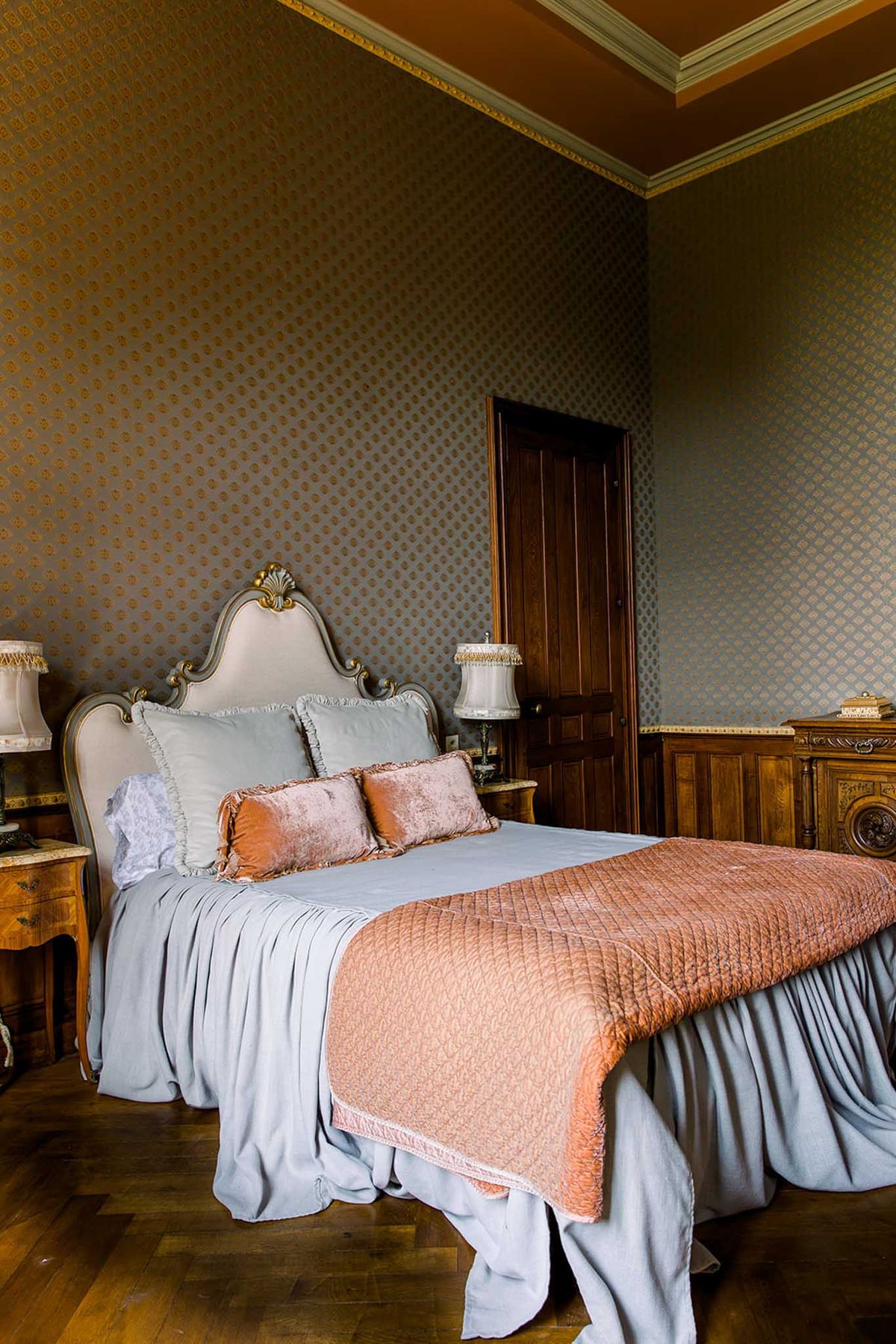 Chateau bedroom with Louis XV headboard, damask wallpaper, and herringbone parquet floor