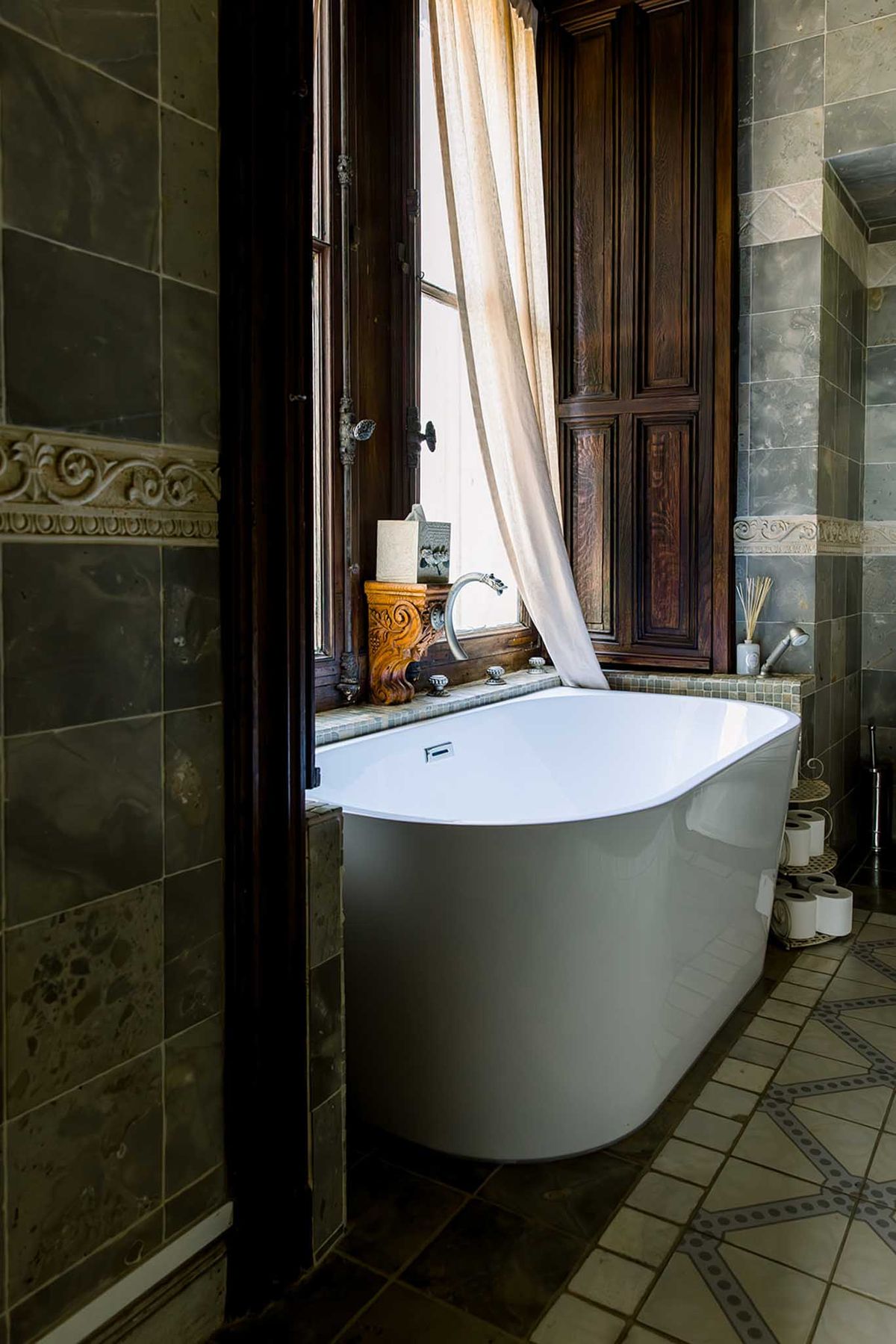 Chateau bathroom with freestanding tub, green-grey marble tiles, and carved stone border detail