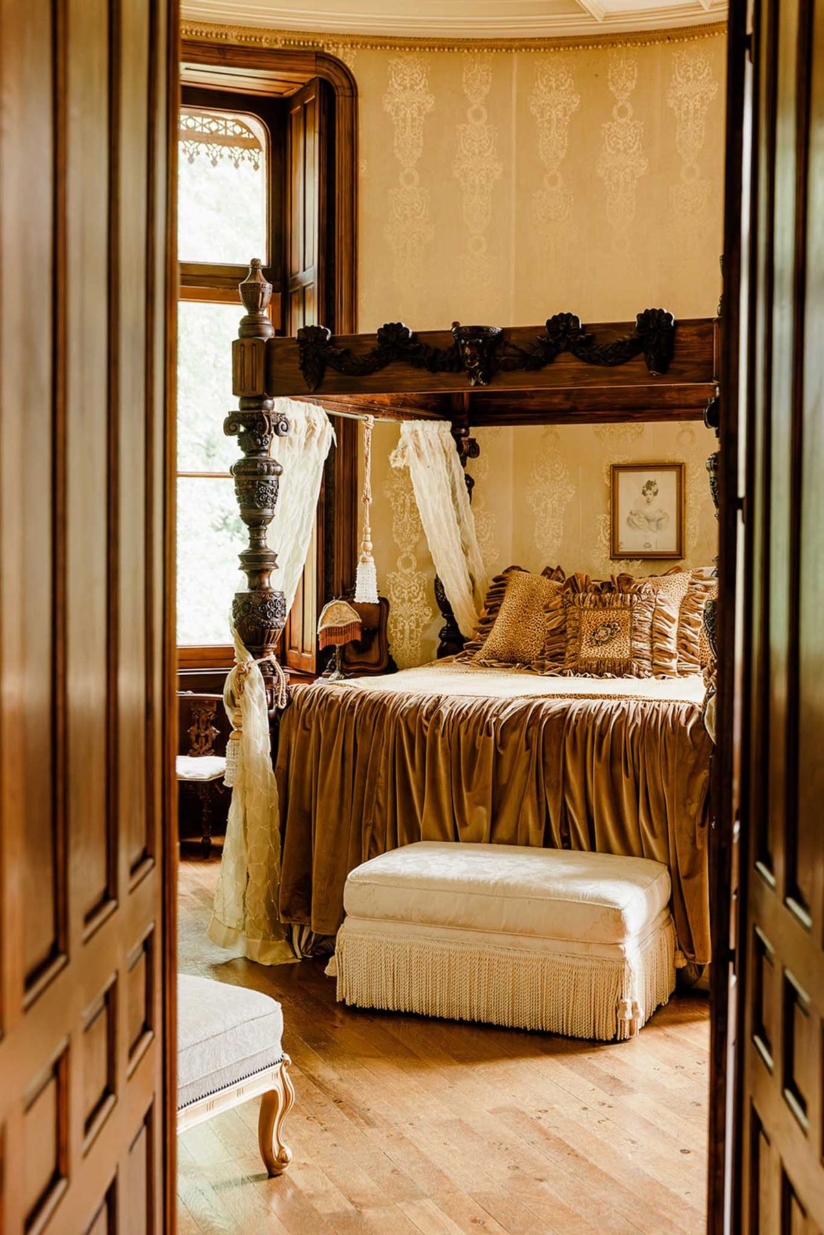Ornate chateau bedroom with carved four-poster bed, lace canopy, gold satin, and damask wallpaper